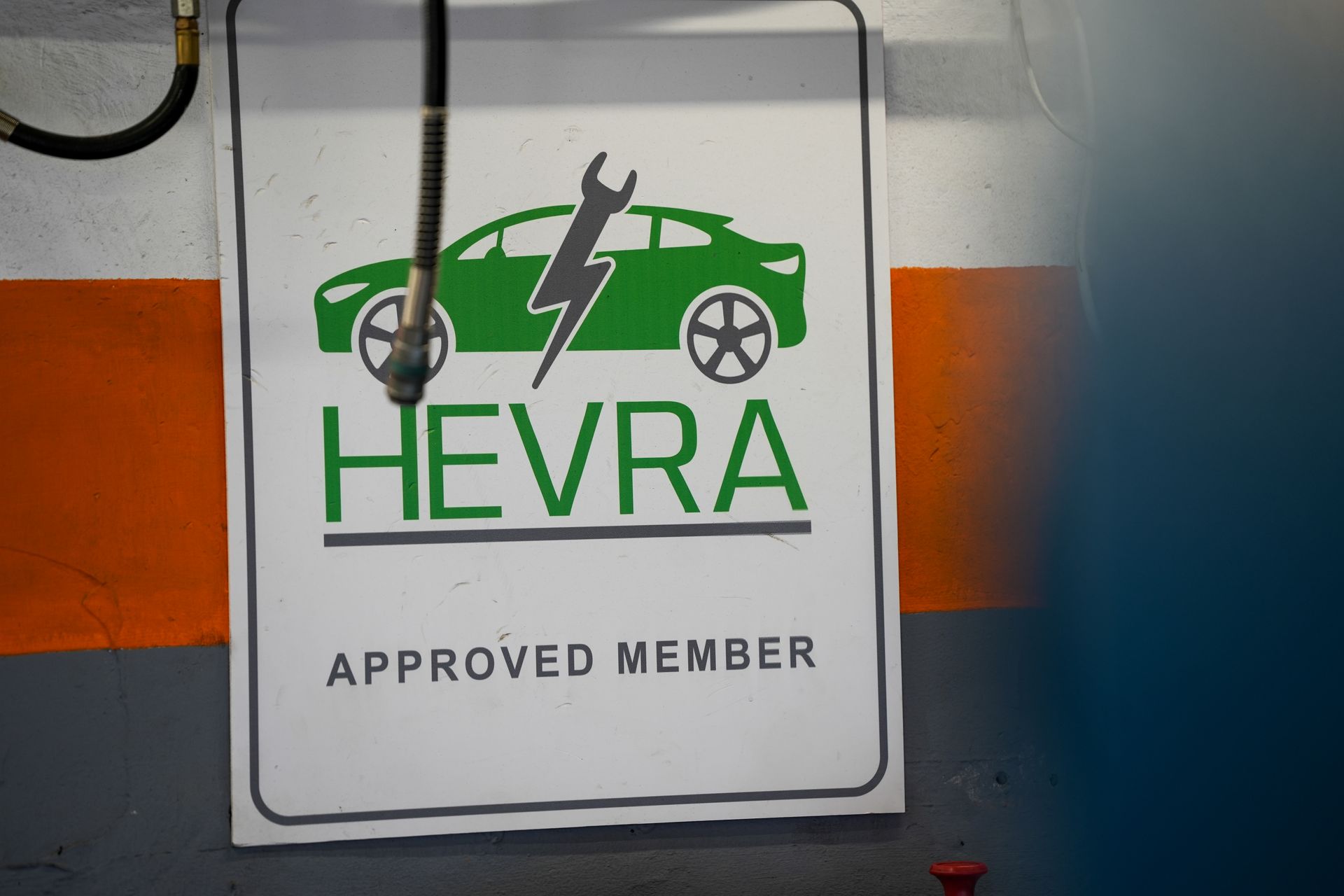 Hands in bright orange gloves hold a black car diagnostic tool with lit indicator lights inside a vehicle.