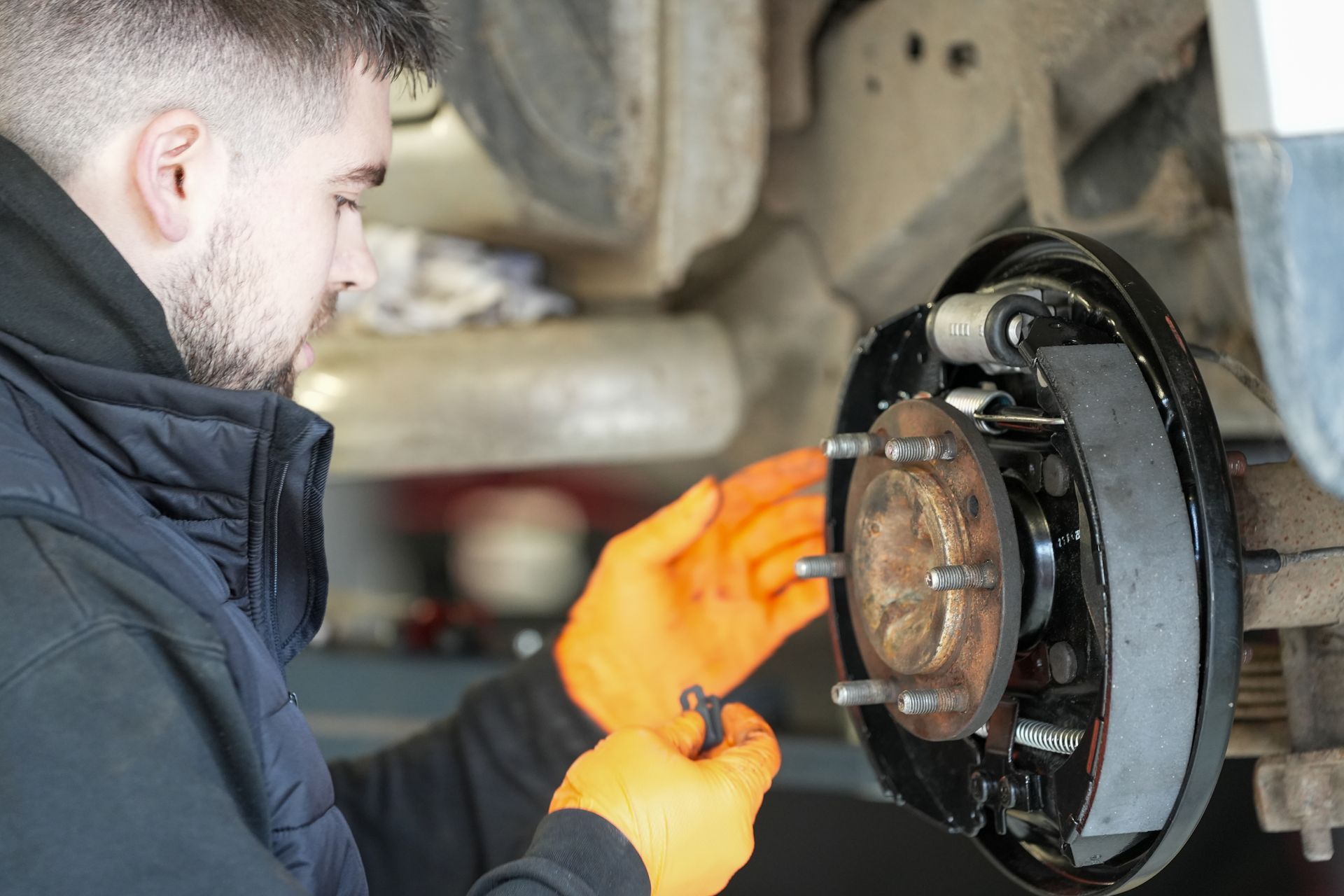 A person holding a handheld diagnostic scanner while inspecting a black car in an automotive garage.
