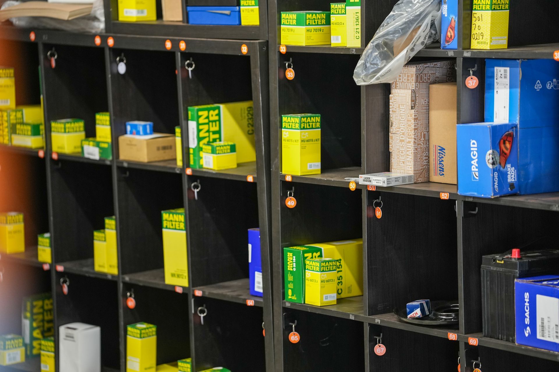 A mechanic wearing an Auto Bliss black t-shirt works under a car raised on a hydraulic lift in a garage.