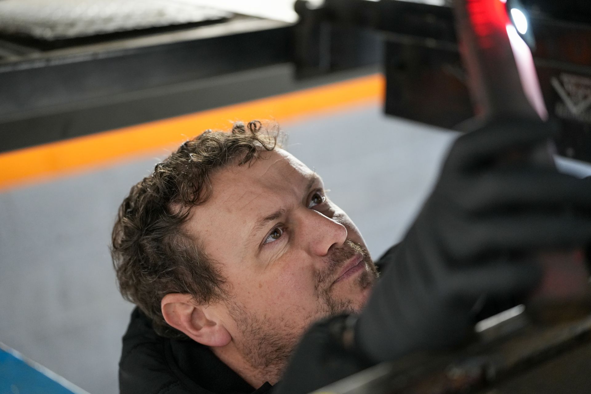 A person holding a handheld diagnostic scanner while inspecting a black car in an automotive garage.