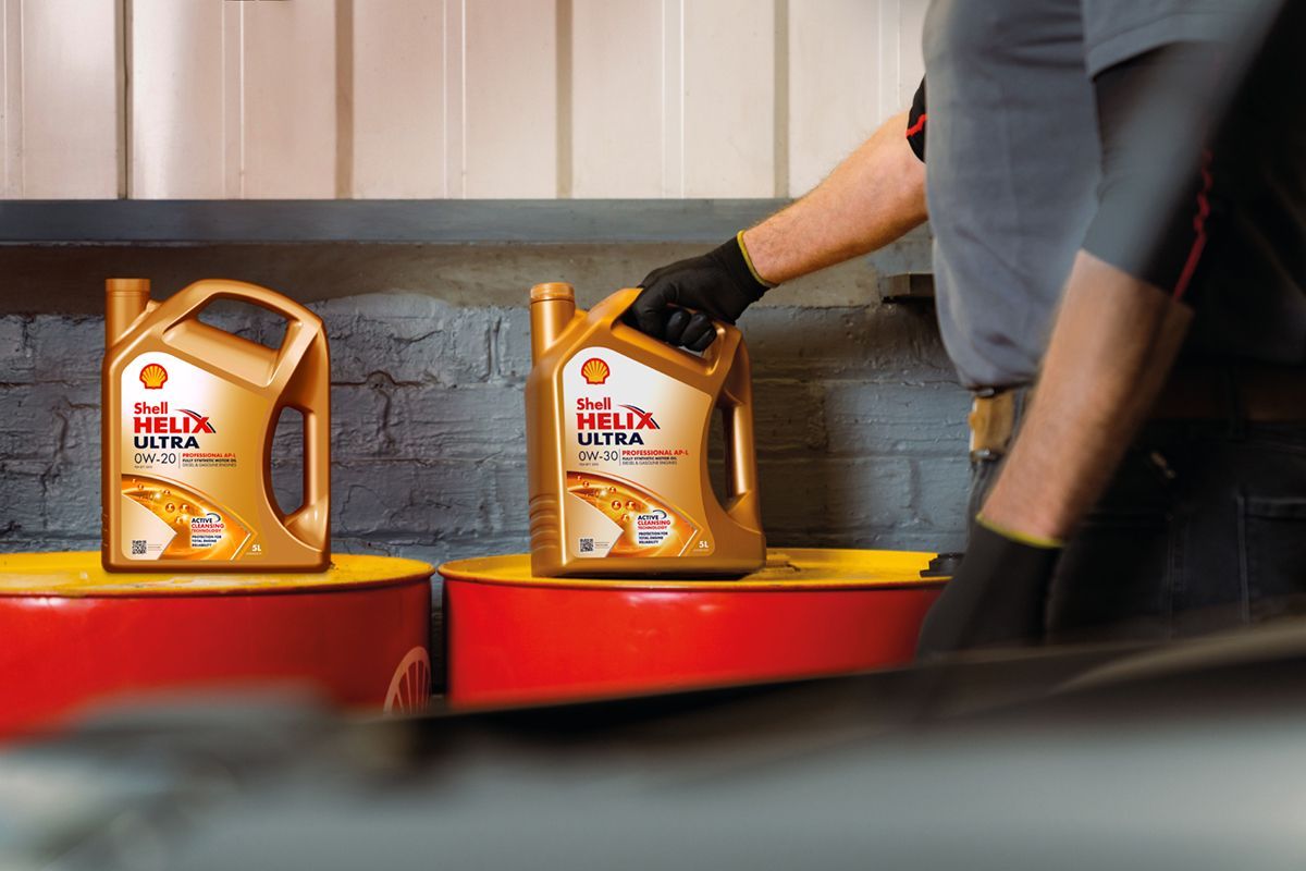 Hands in bright orange gloves holding an automotive diagnostic scanner with lit indicator lights on a dark surface.
