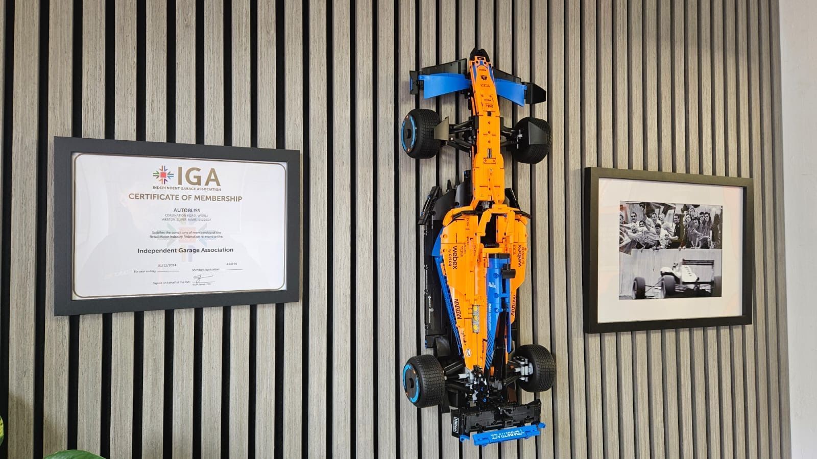 A person holding a handheld diagnostic scanner, reviewing the interface next to a black car in an automotive garage.