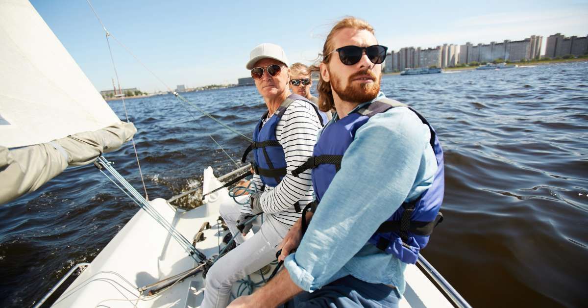 Group of men in life jackets and sunglasses sitting on a yacht looking forward while on a sailing tour.