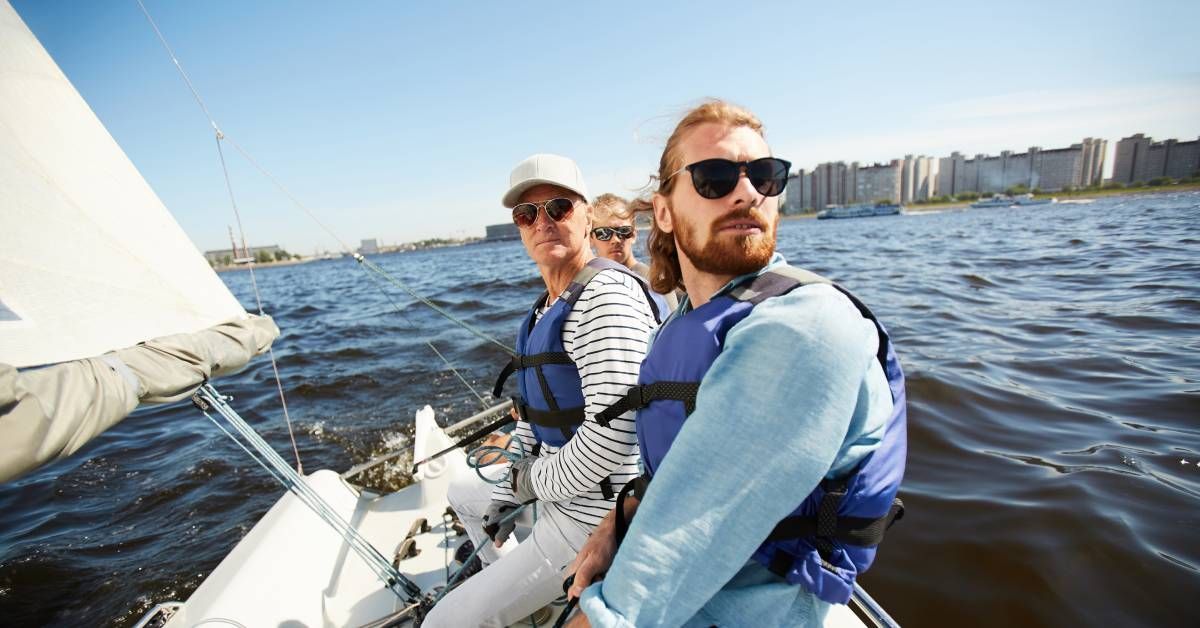 A group of serious men in life jackets sit in a row on a yacht, attentively looking around as they e