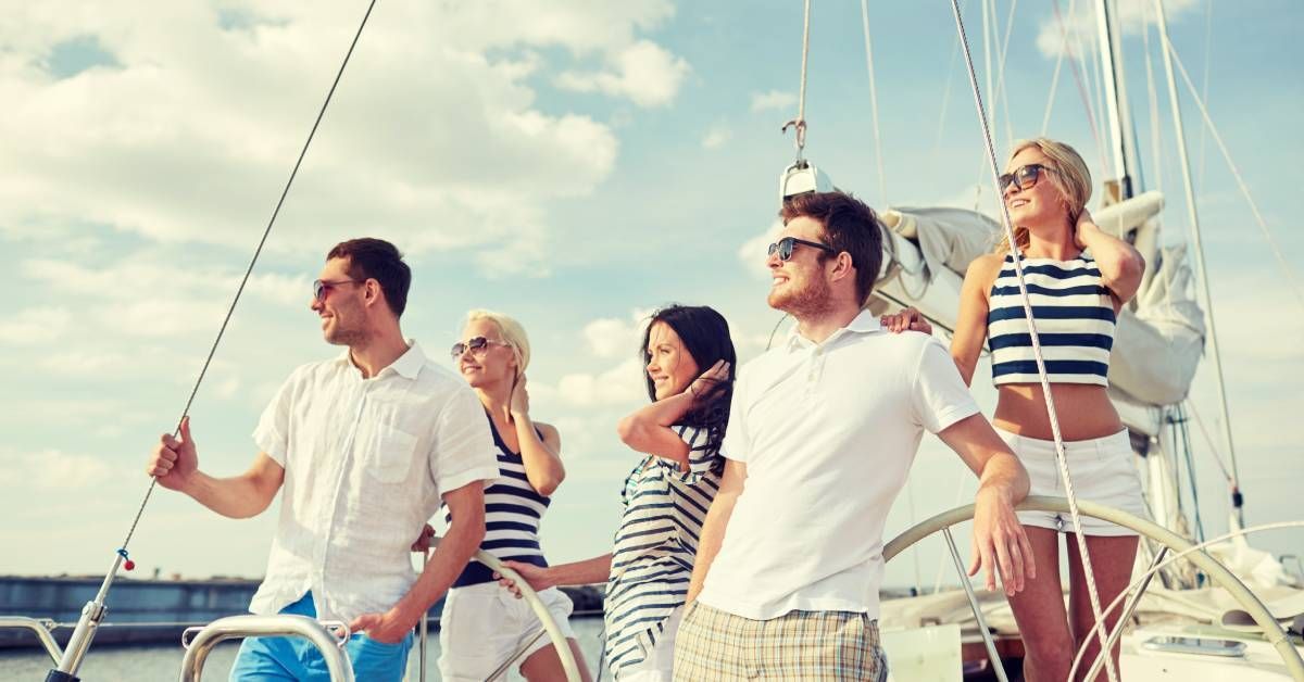 A group of smiling friends enjoying their time on a yacht under clear blue skies, with the sun shining brightly.