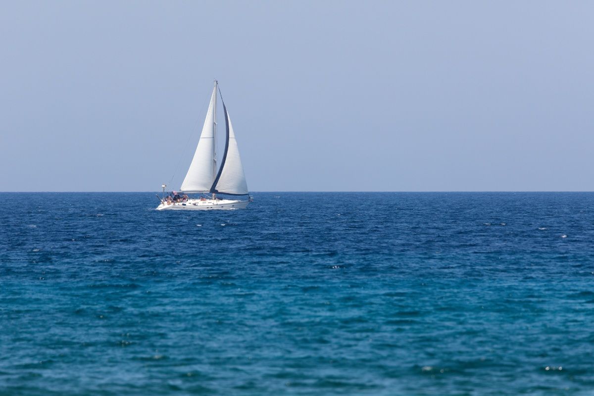 A distant sailboat gliding peacefully across calm waters on a sunny day without a cloud in the background.