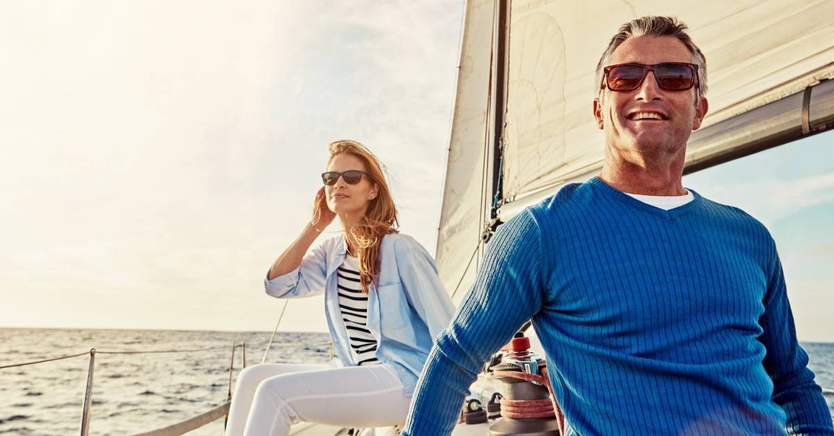 A mature couple smiling and relaxing while sailing on a luxury yacht in the ocean, enjoying their travel.