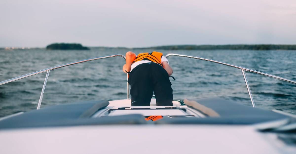 A seasick man leaning over the side of a yacht with choppy ocean waters and cloudy skies in the back