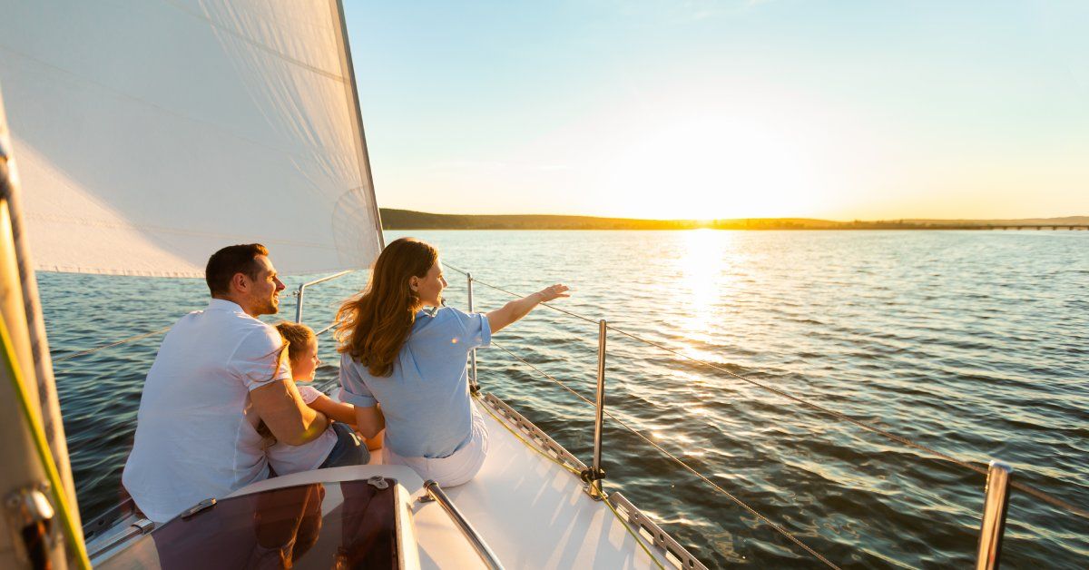 A woman, man, and little girl sitting at the front of a sailboat with stainless steel guardrails.