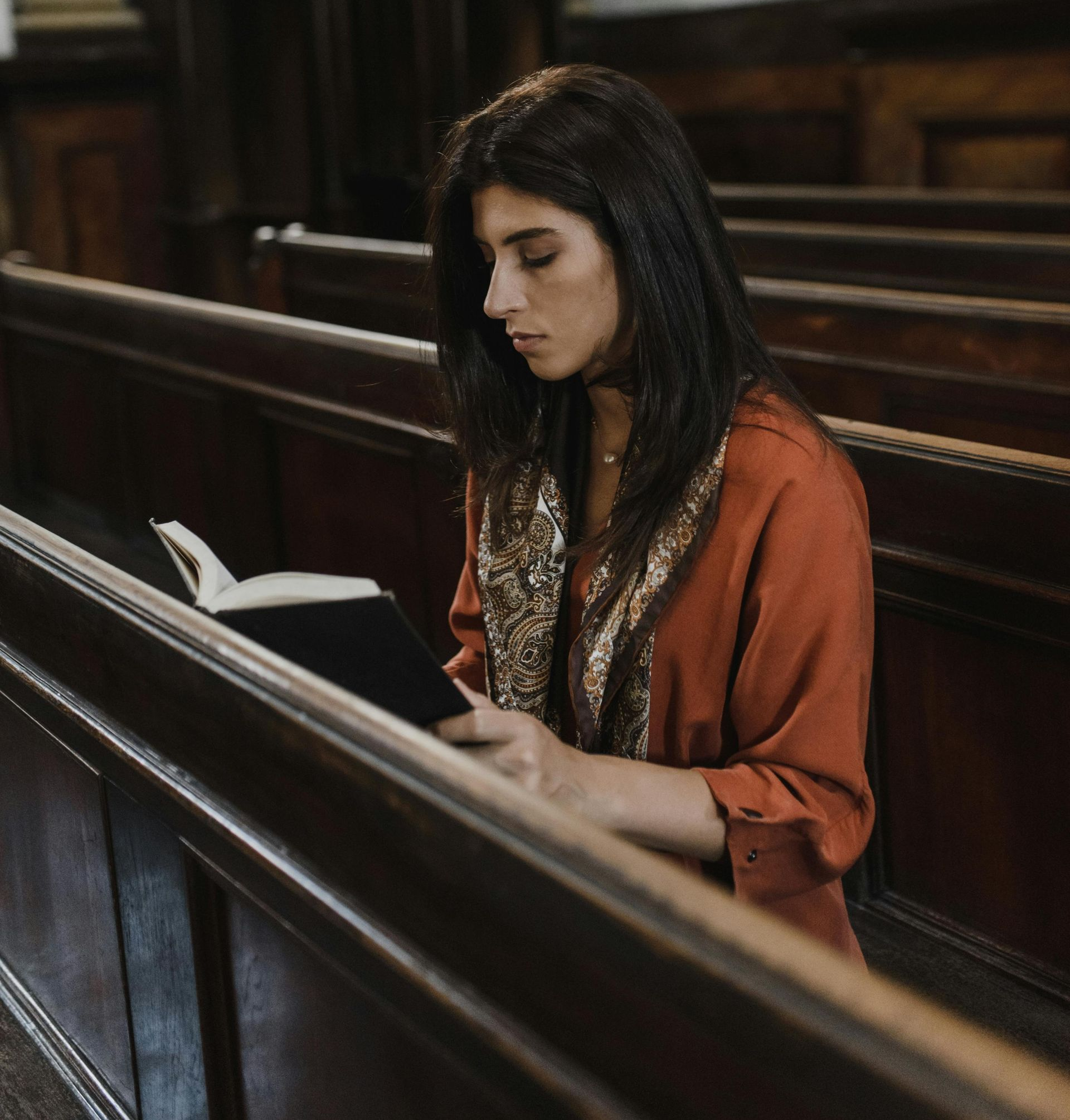 Woman in black veil places a white rose on a casket with flowers. Church setting.