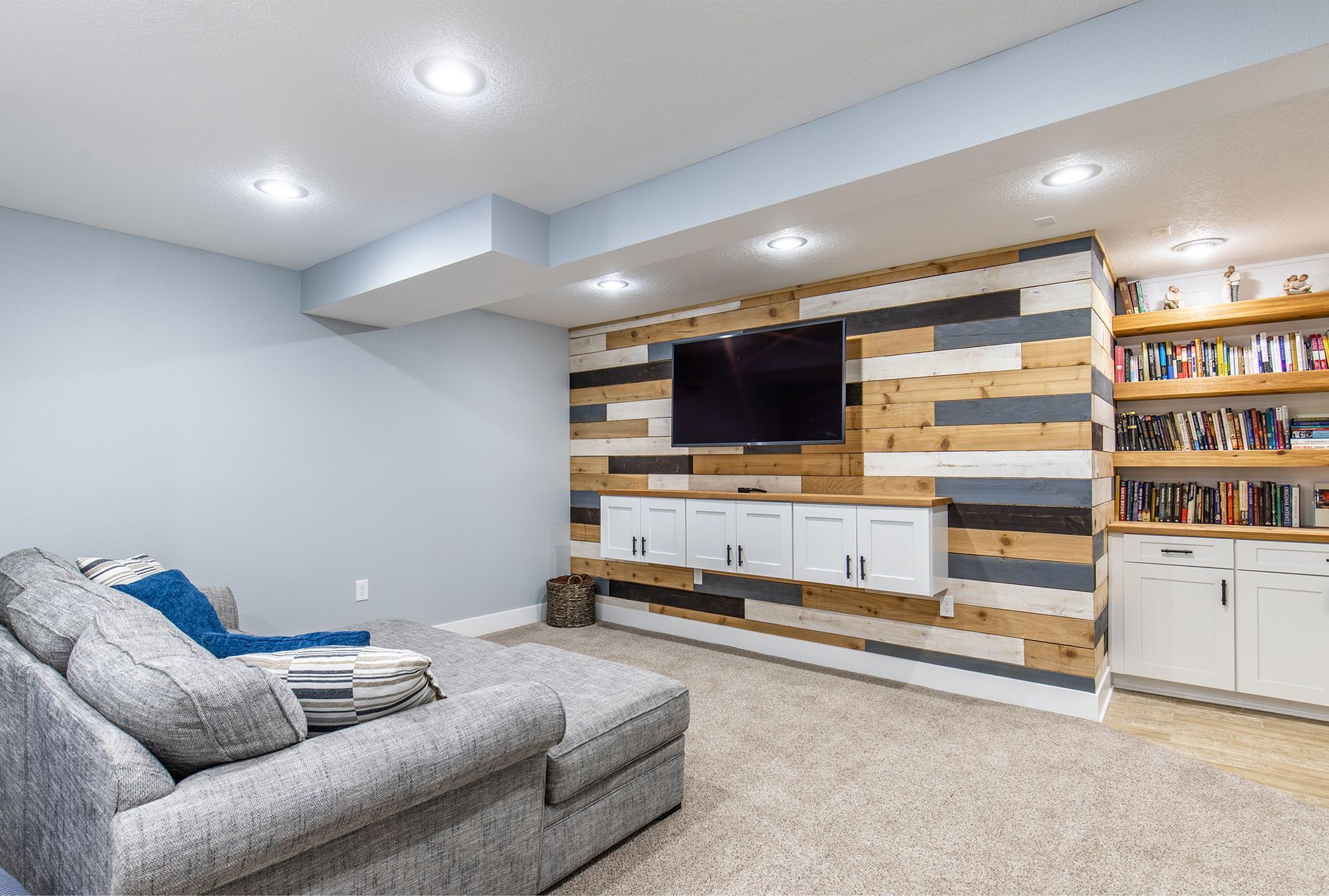 An added living room in a finished basement with a wooden wall and a flat screen tv.