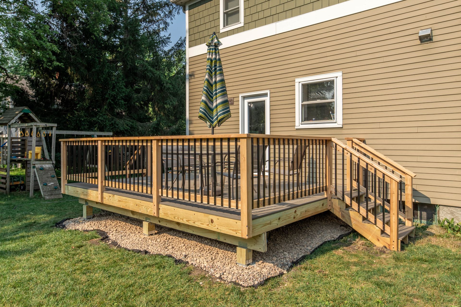 A wooden deck with stairs leading up to it is in the backyard of a house.