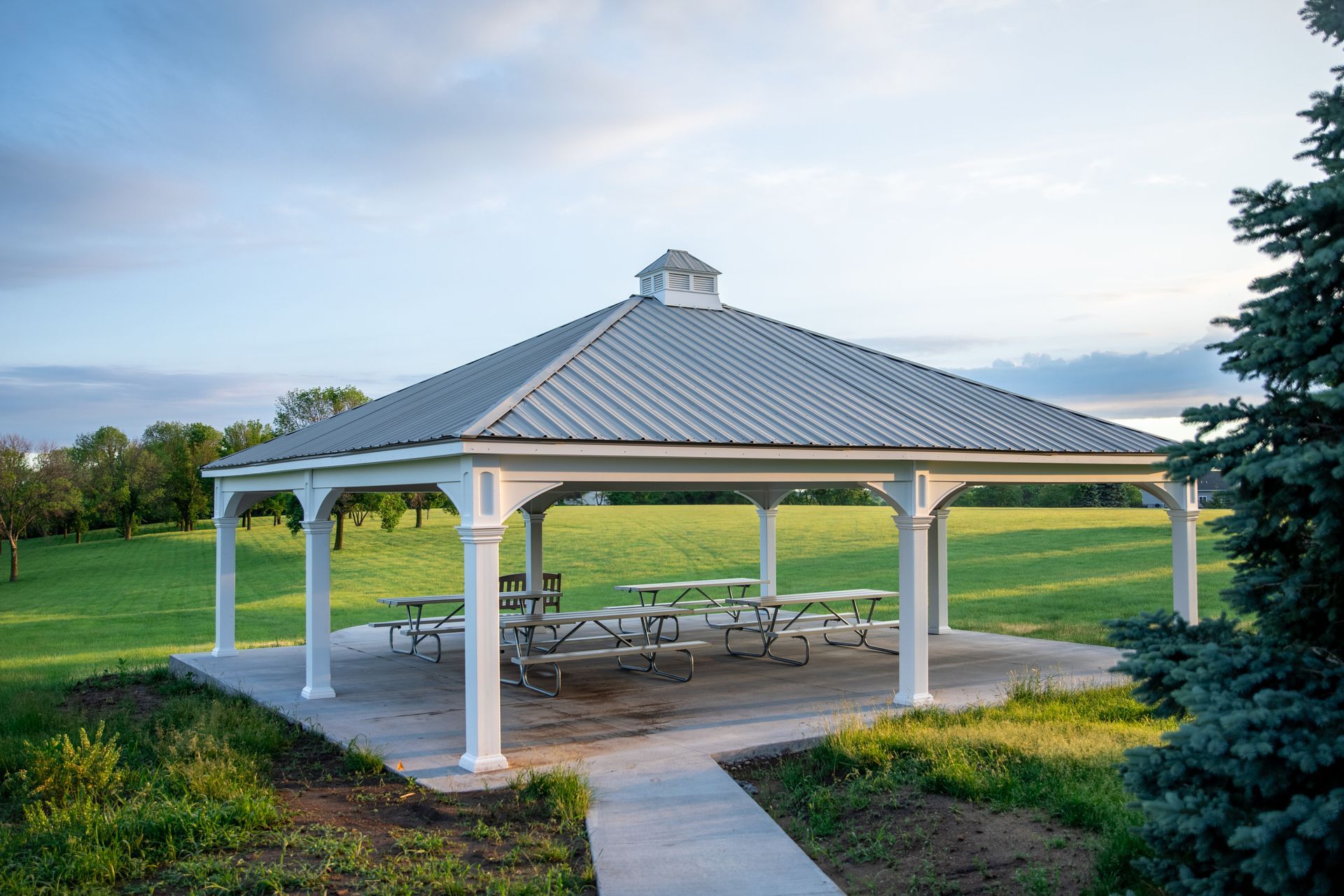 A white gazebo with a metal roof and picnic tables in a park.