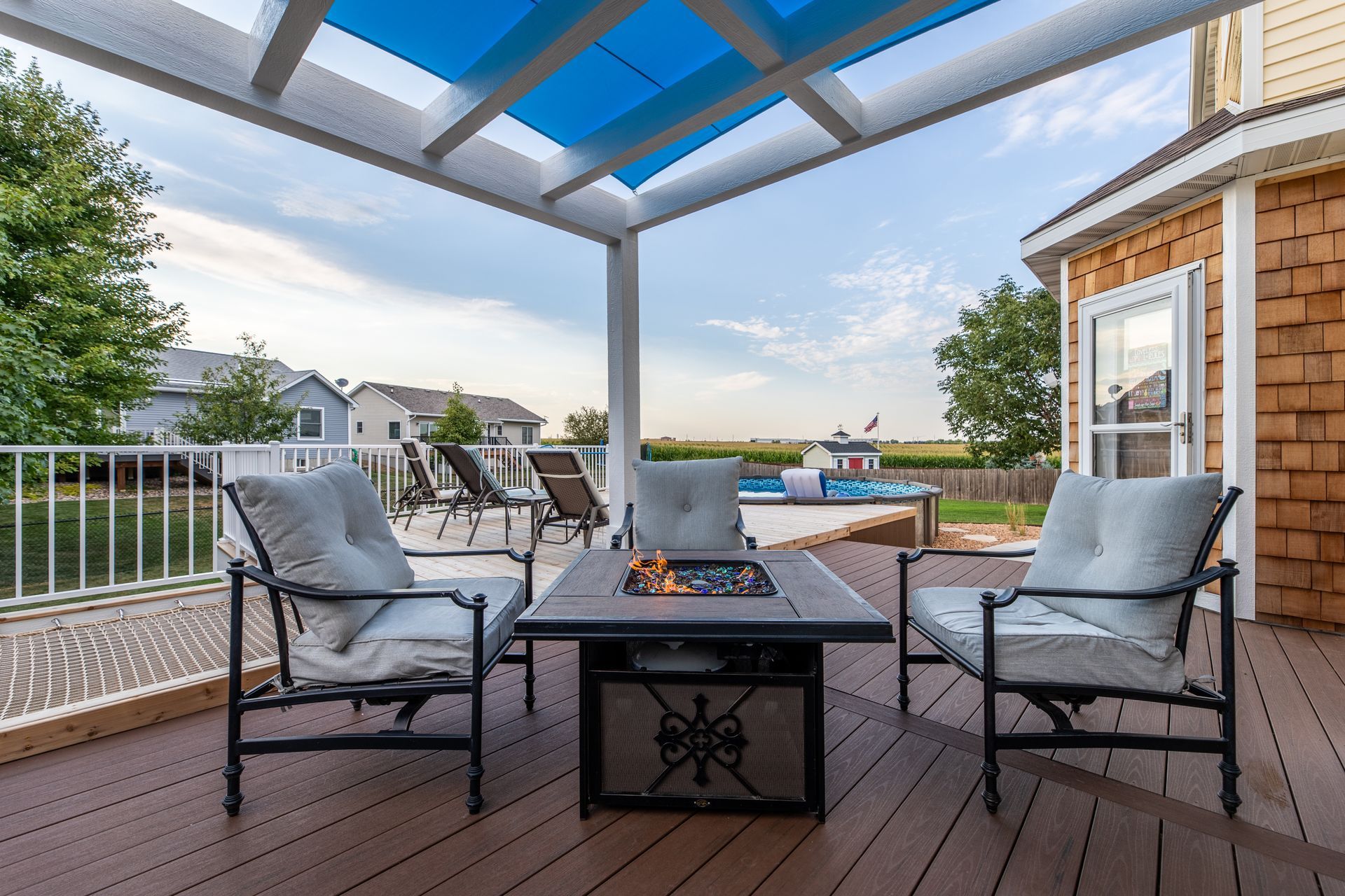 A deck with a fire pit and chairs under a blue canopy.