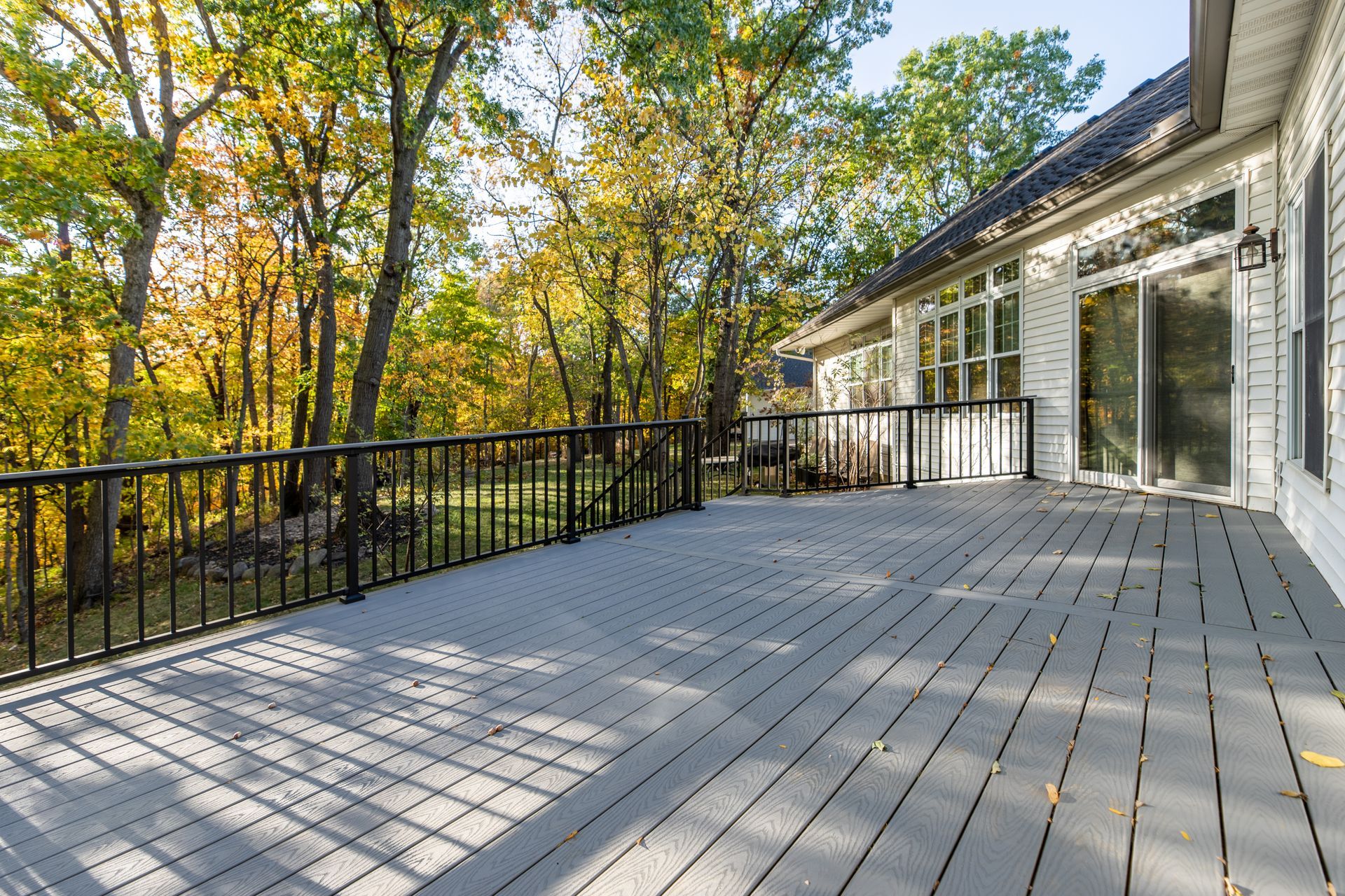 There is a large composite deck with a railing and trees in the background.