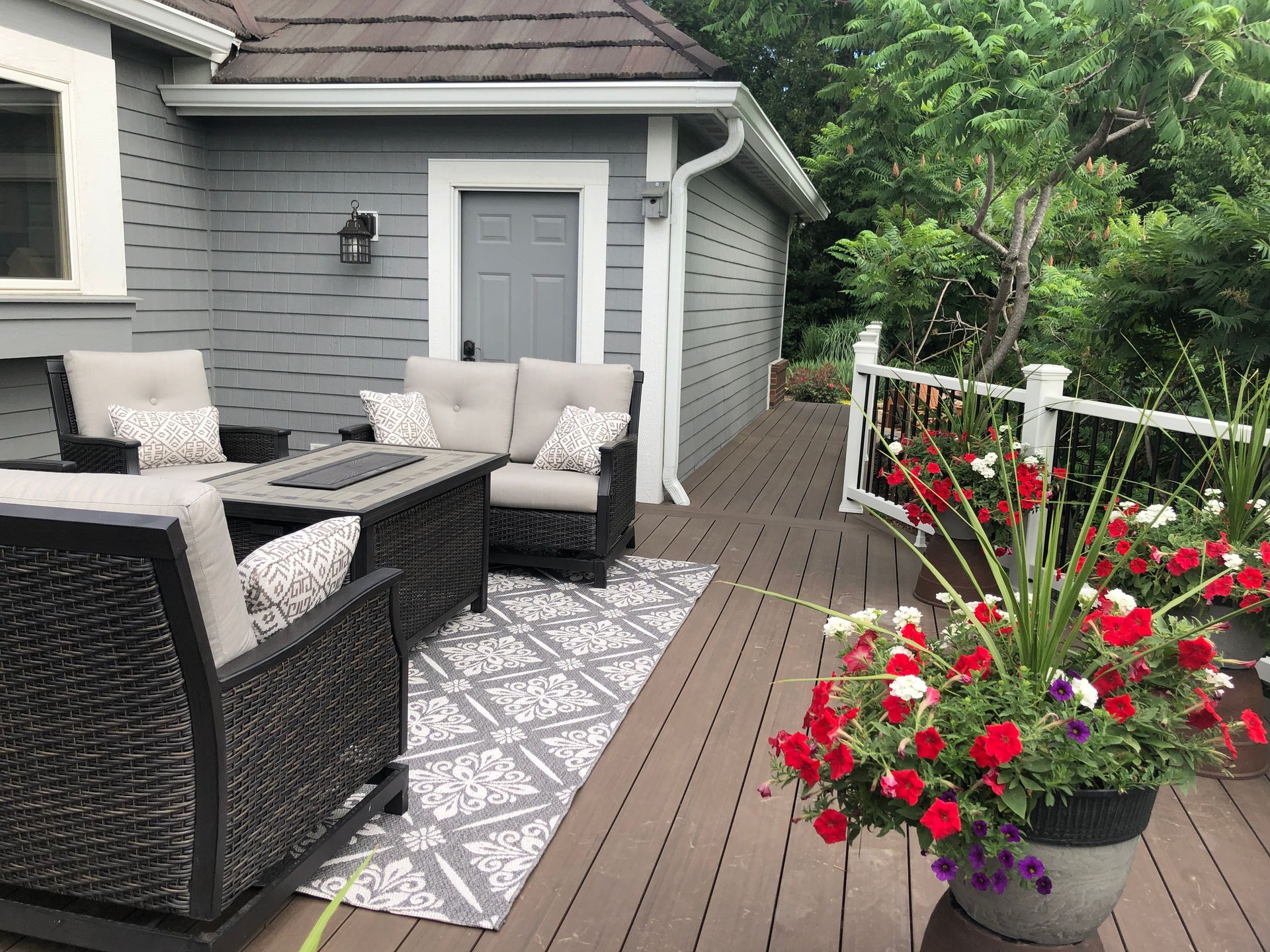 A deck with a couch , chairs , table and potted flowers.