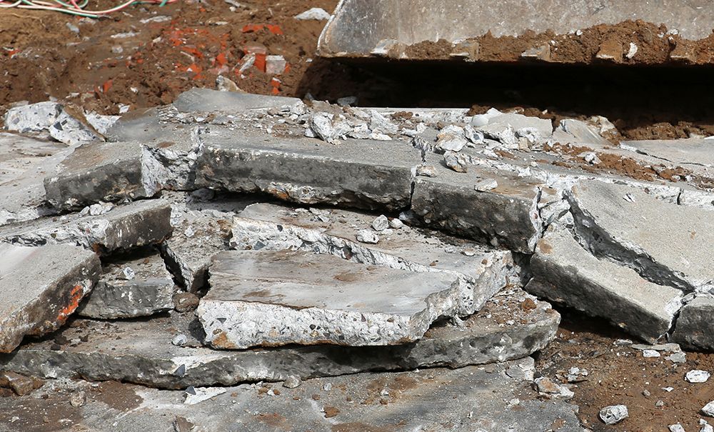A pile of broken concrete slabs and rubble sits on a dirt construction site.