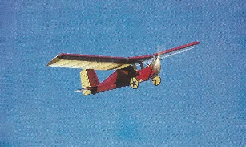 Red and beige single-engine airplane in flight against a blue sky.