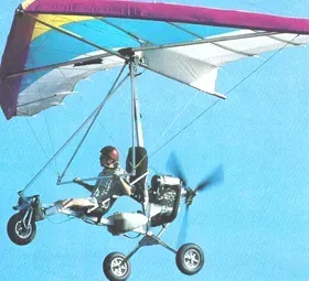 A person flying a motorized hang glider with a blue and purple wing against a blue sky.