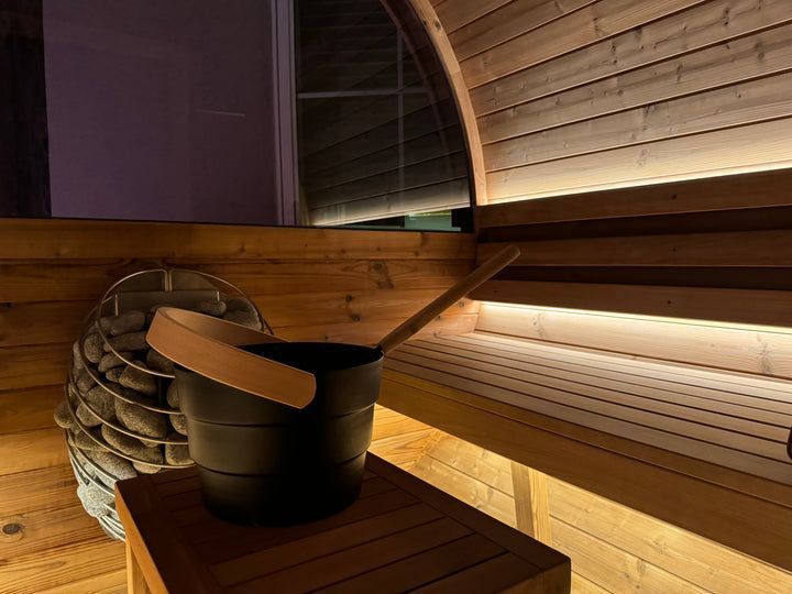 A black bucket with a wooden ladle is sitting on a wooden table in a wooden sauna.