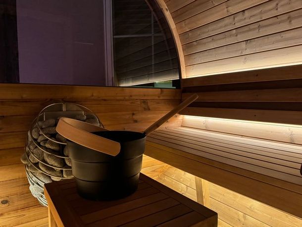 A black bucket with a wooden ladle is sitting on a wooden table in a wooden sauna.