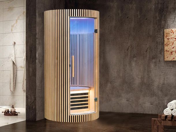 A wooden indoor luxury sauna is sitting in the corner of a bathroom next to a shower.