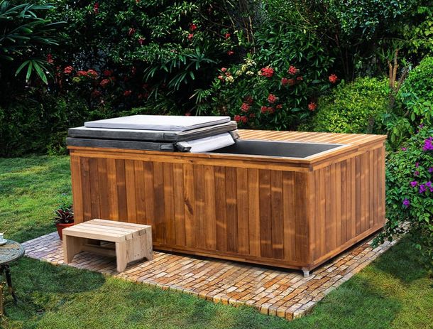 A wooden luxury plunge tub is sitting in the middle of a lush green garden.