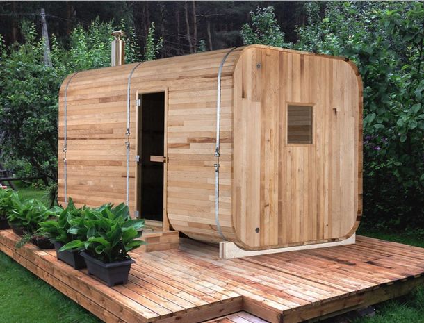 A wooden sauna is sitting on a wooden deck surrounded by plants.