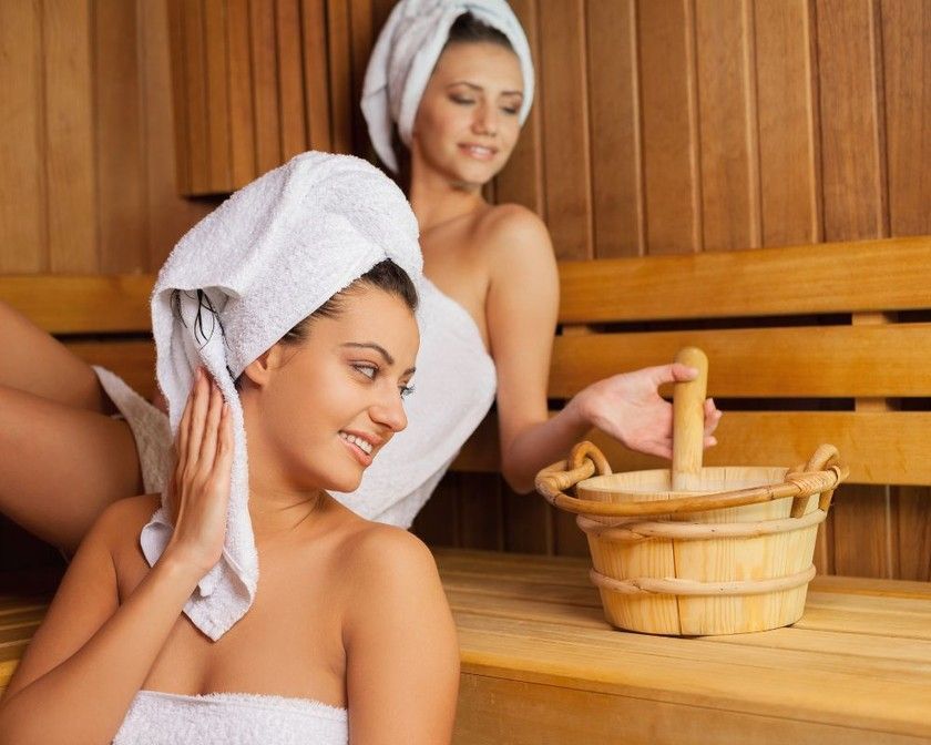 Two women wrapped in towels are sitting in a sauna.