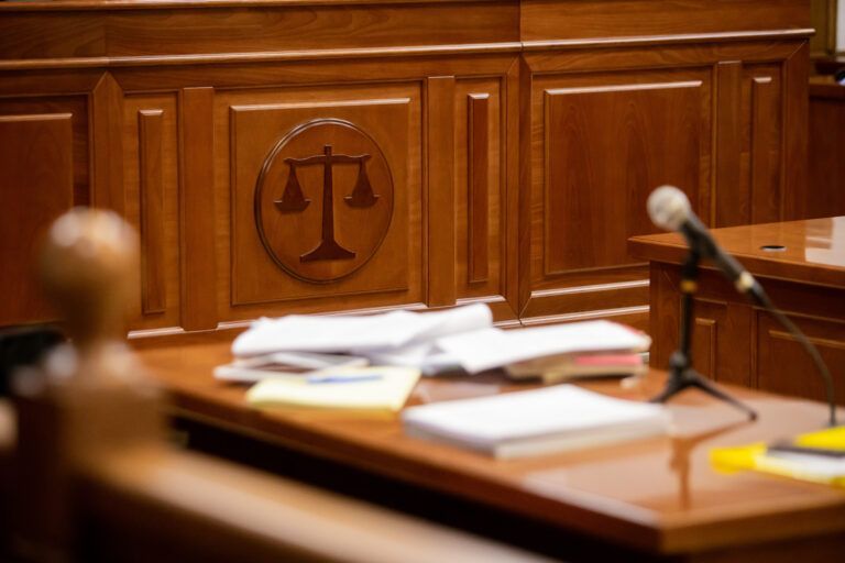 Wooden courtroom with scales of justice emblem; desk with papers and microphone.
