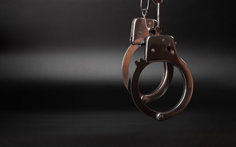 Silver handcuffs hanging against a dark background.