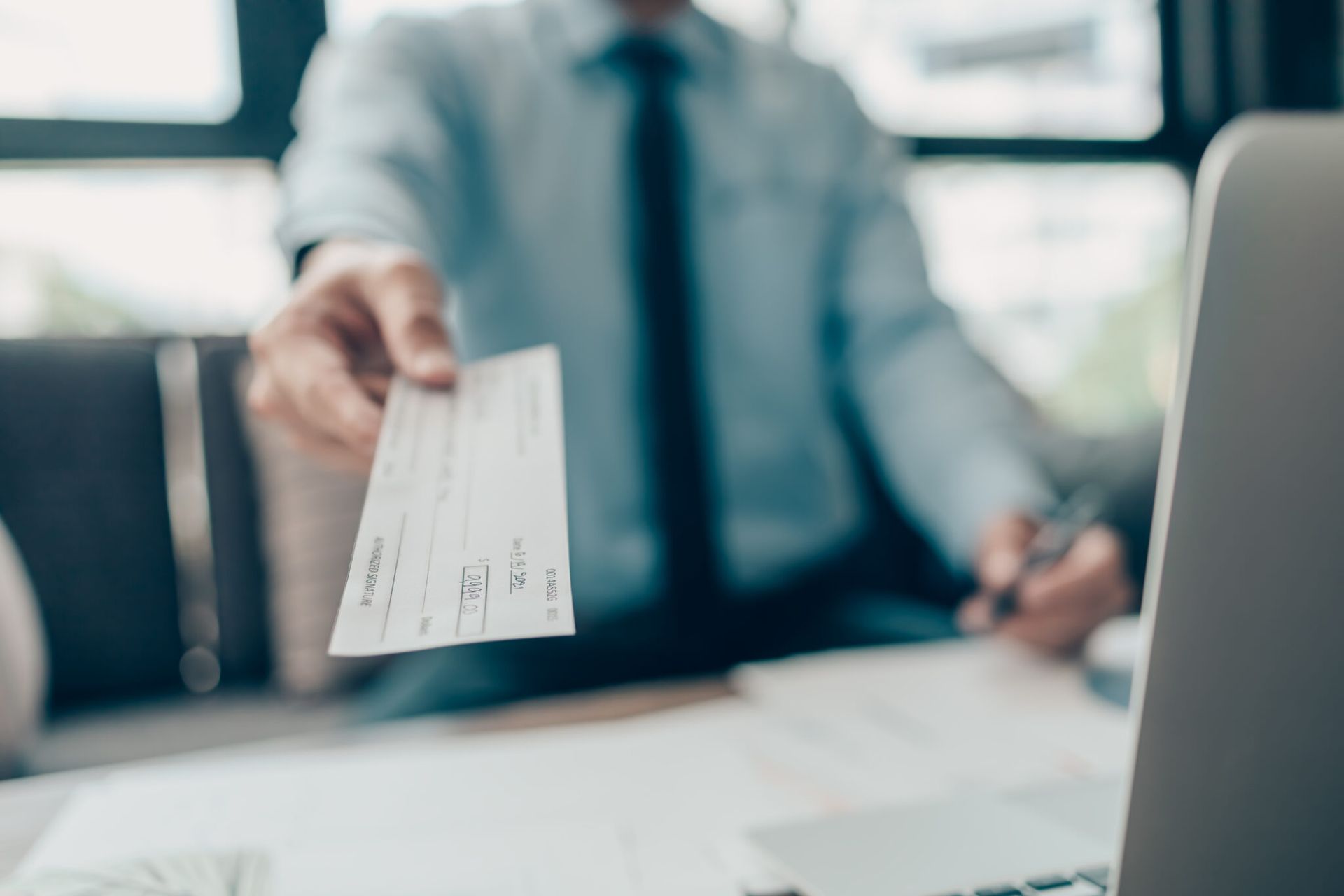 Person in blue shirt and tie holding out a signed check.