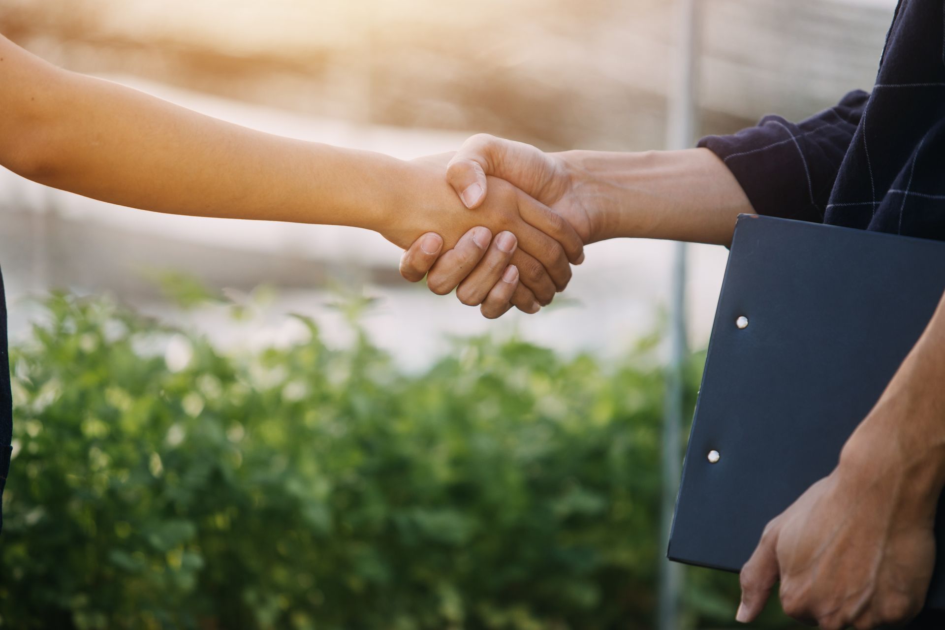 Ein Mann und eine Frau geben sich die Hand und halten dabei ein Klemmbrett in der Hand.