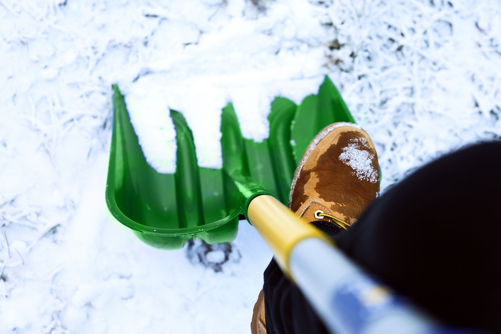 Eine Person schaufelt Schnee mit einer grünen Schaufel.