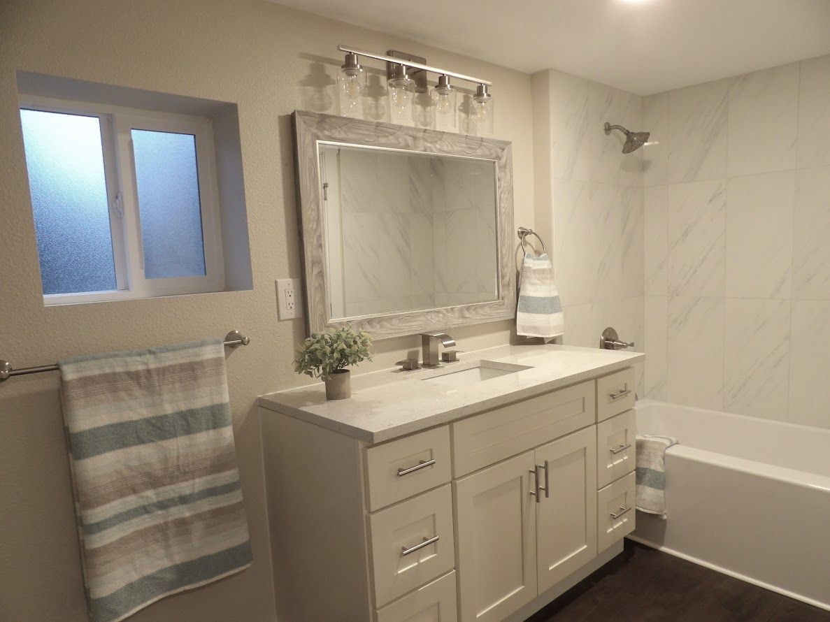 Bathroom with white vanity, large mirror, tub, and window.