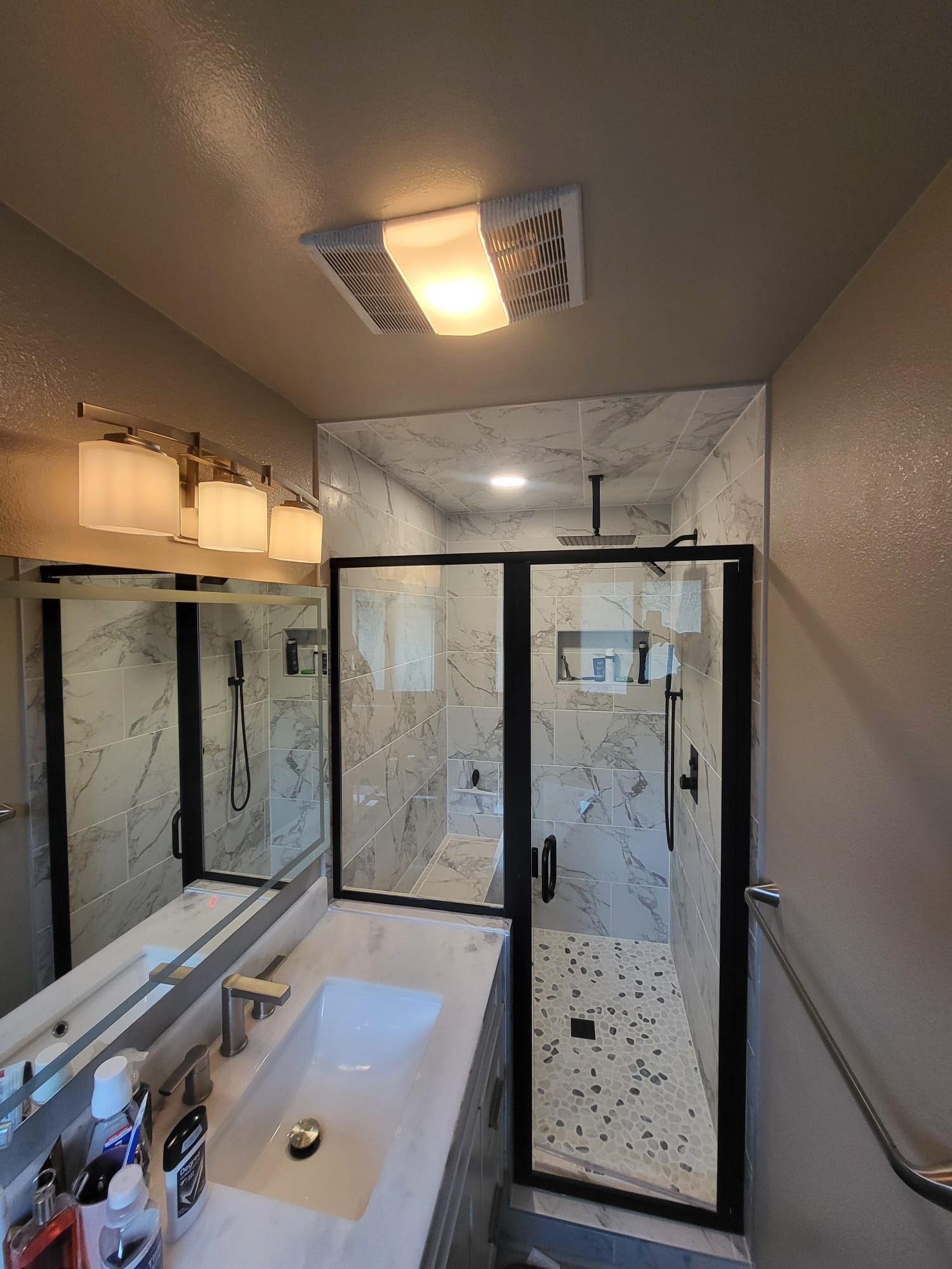 Bathroom with marble-look tile, black framed shower, overhead light, and vanity with mirror.