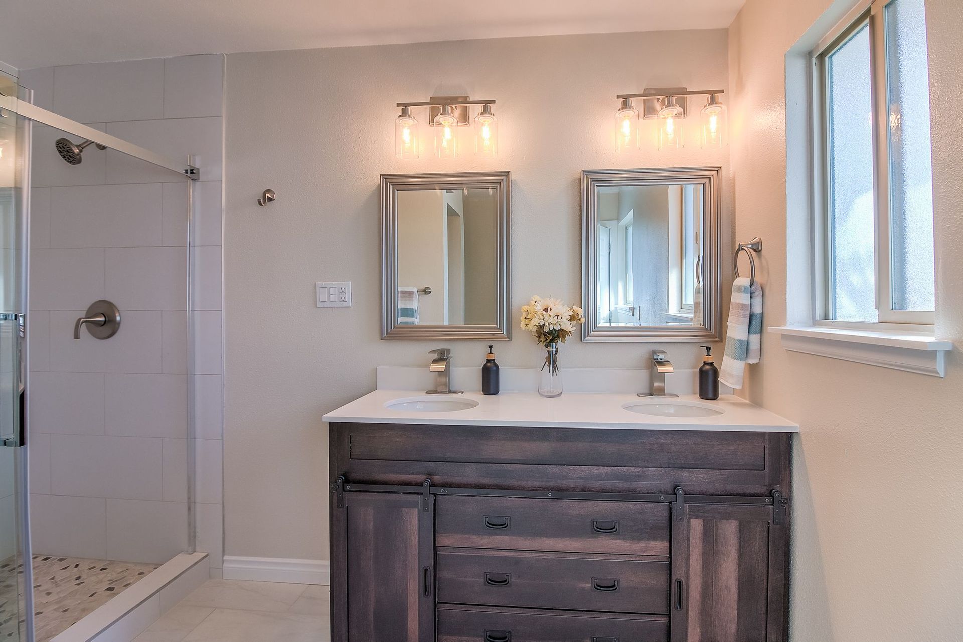Bathroom with double vanity, two mirrors, and a shower, neutral colors.