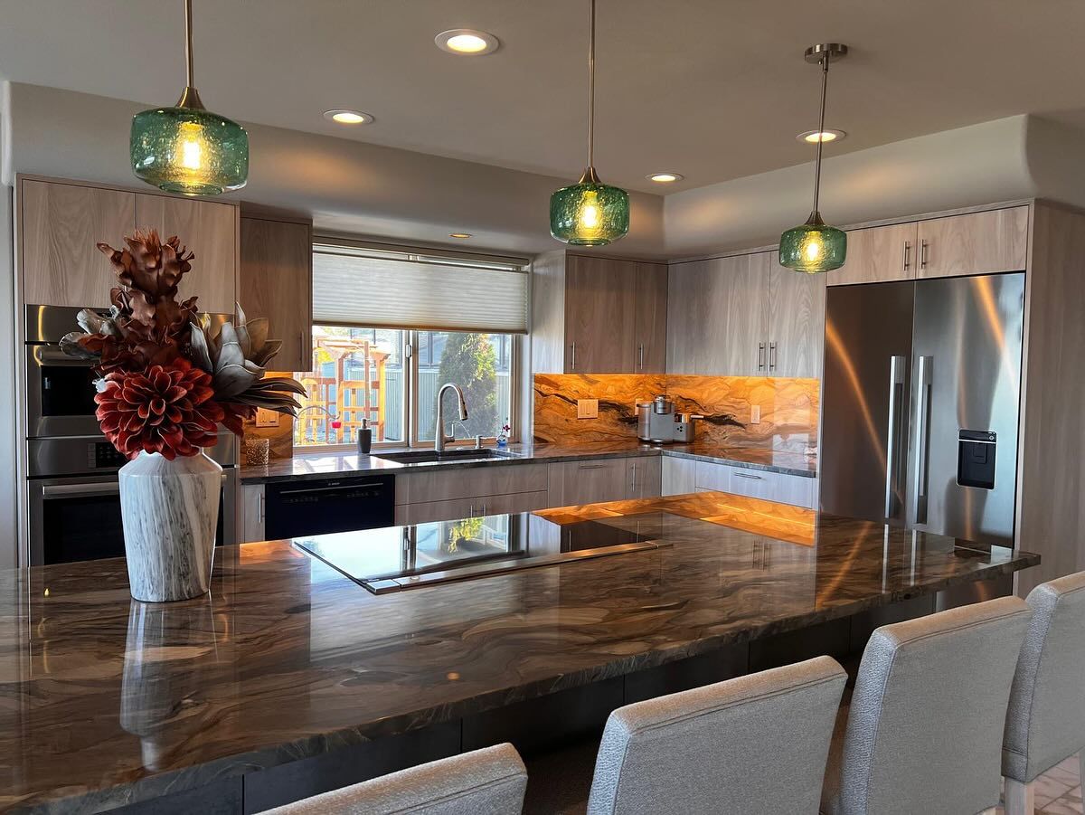 Modern kitchen with granite island, wood cabinets, and green pendant lights.
