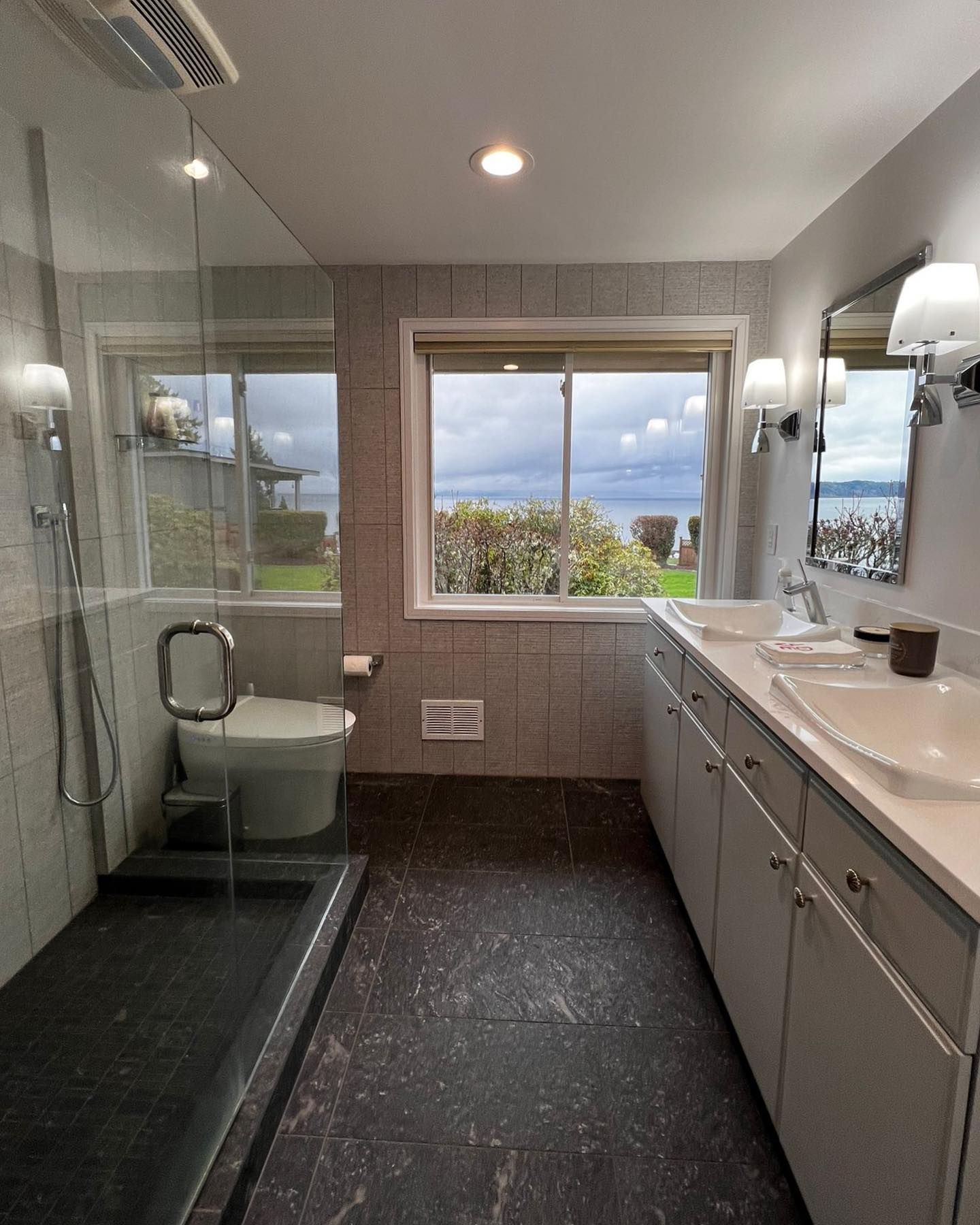 Bathroom with ocean view, featuring a shower, toilet, and double sink vanity.