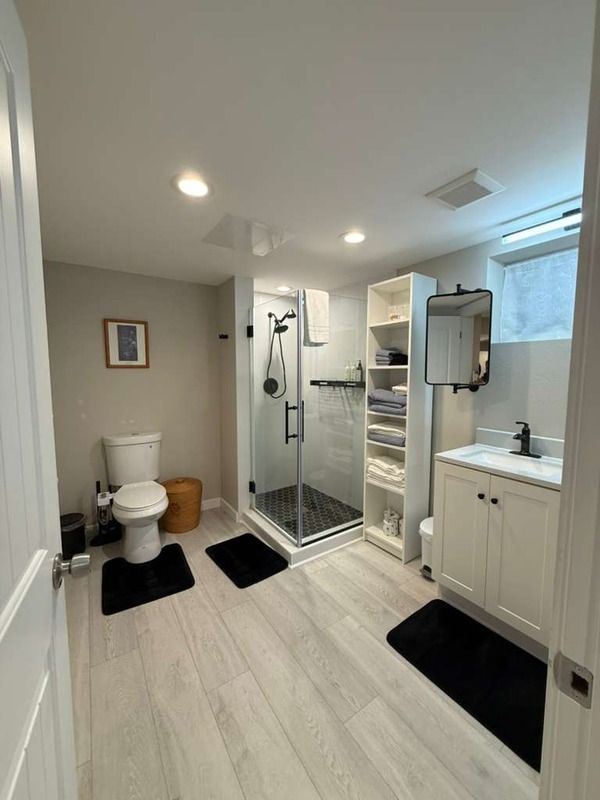 Modern bathroom with white and gray tones. Features a shower, toilet, vanity, and shelving. Black accents.
