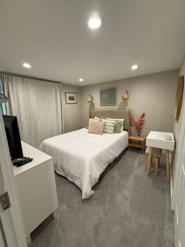 Bedroom with bed, nightstand, and dresser; neutral colors with gray carpet.