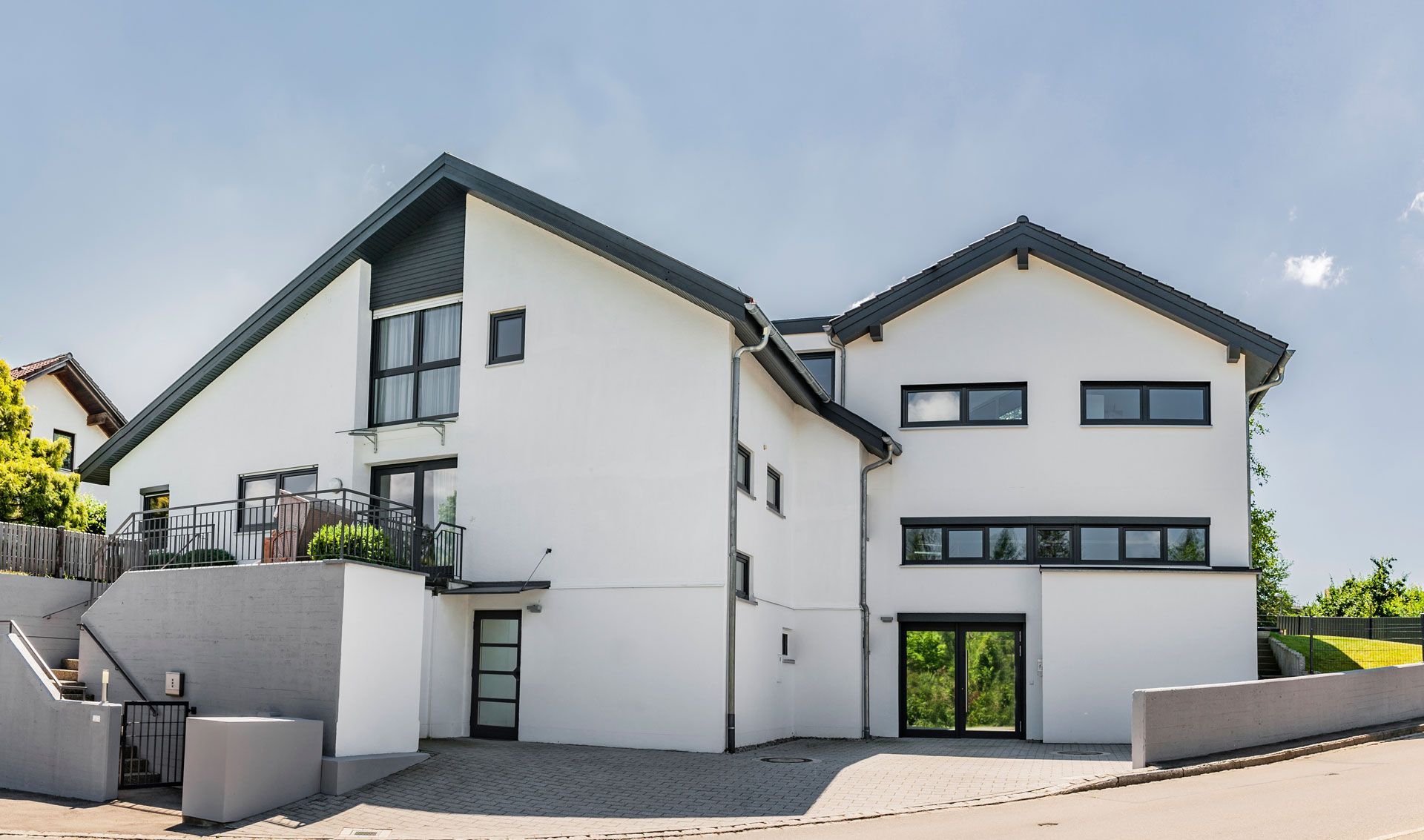 Modern white building with dark trim, windows, and two-story structure on a sunny day.