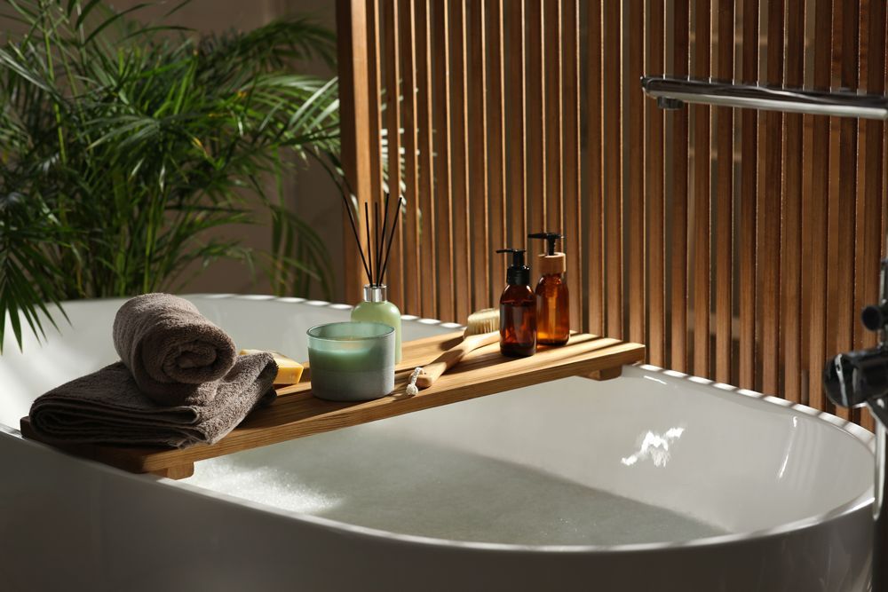 a bathtub with a wooden tray with candles and towels on it