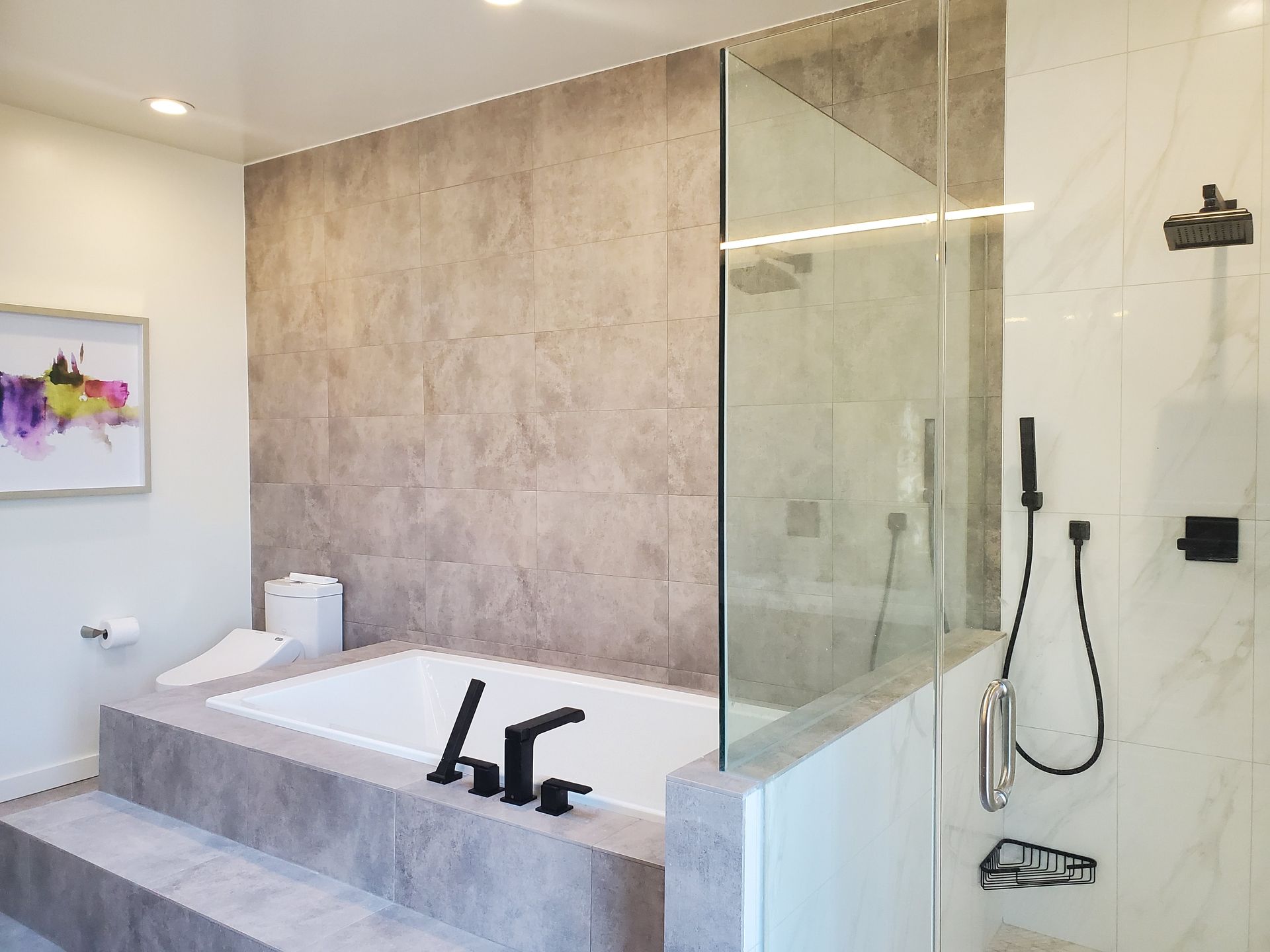 Modern bathroom with a bathtub, shower, and gray tile walls. Black fixtures and a glass shower door.