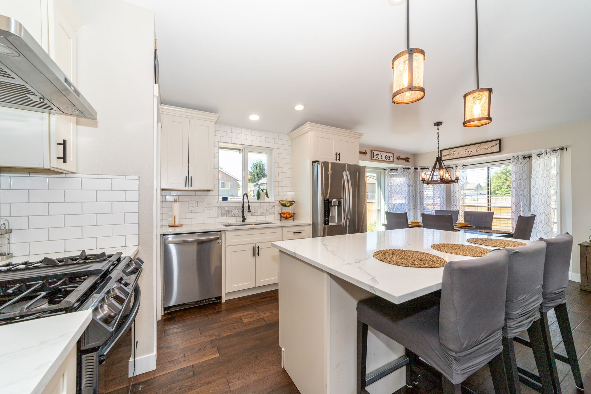 Modern white kitchen with island, stainless steel appliances, dark wood floors, and pendant lights.