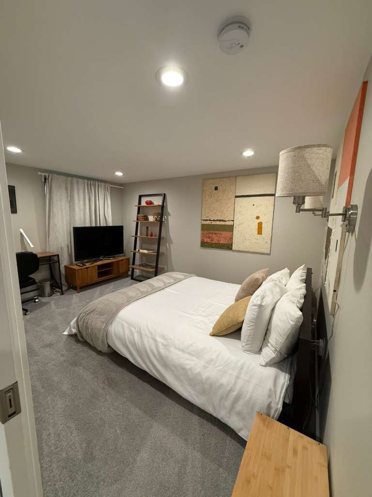Bedroom with bed, television, artwork, and a small wooden table.