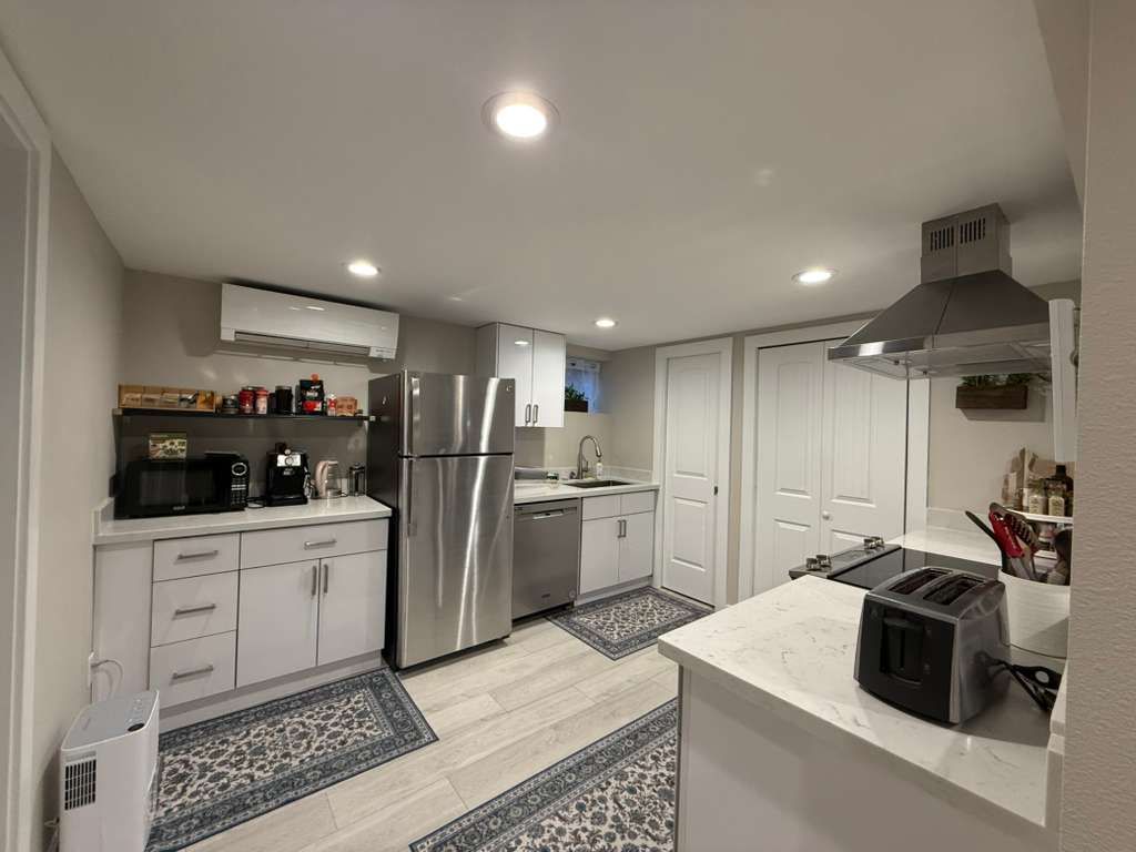 A modern kitchen with stainless steel appliances, white cabinets, and countertops. Includes a toaster and rug.