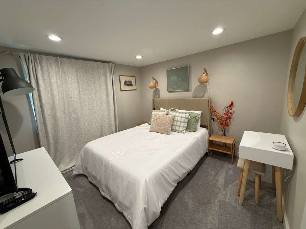Bedroom with a bed, dresser, nightstand, and vanity. Gray walls, carpet, and curtains.