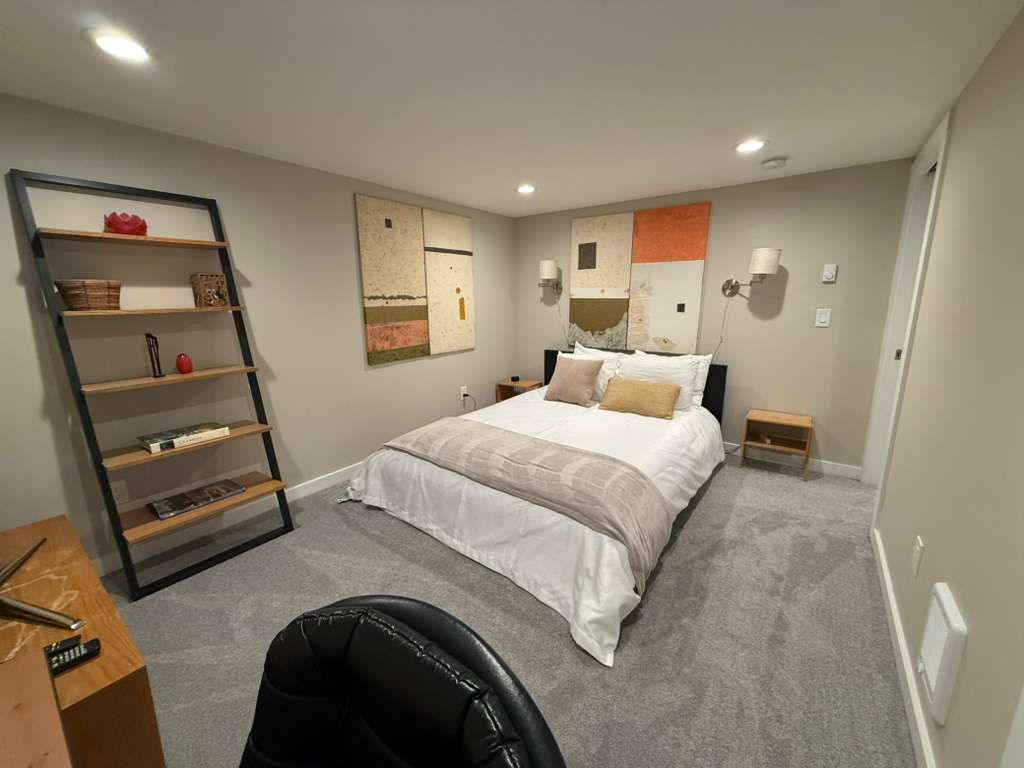 Bedroom with bed, rug, shelves, artwork, and desk.