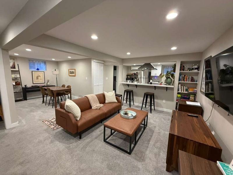 Living room with brown leather sofa, open kitchen, dining area, and TV on the wall.